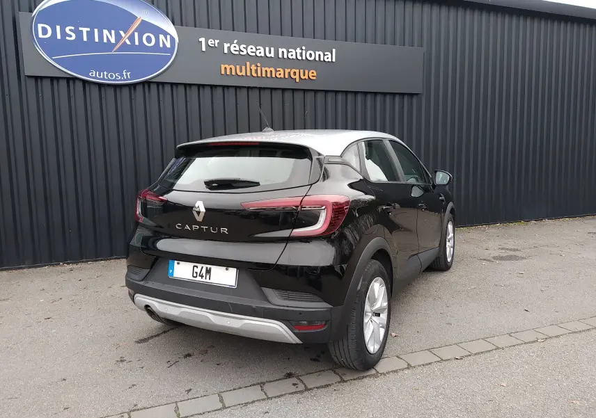 Vue 3/4 arrière droite d'un Renault Captur noir avec toit blanc, garé devant un mur noir avec enseigne Distinxion.