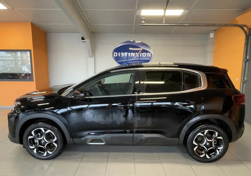 Vue de profil côté gauche d'un Citroën C5 Aircross noir 2024 avec jantes alliage biton 18 pouces en intérieur showroom.