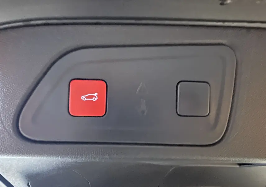 Gros plan sur le bouton rouge d'ouverture du coffre dans l'habitacle du Citroën C5 Aircross noir 2024.