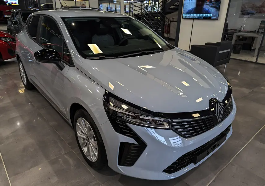 Renault Clio V Blue dCi 100 Gris Rafale vue 3/4 avant en intérieur, avec calandre noire et phares LED distinctifs.