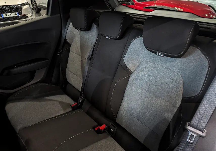 Vue intérieure sur les sièges arrière en tissu bicolore gris et noir de la Renault Clio V 2025, avec ceintures de sécurité visibles.