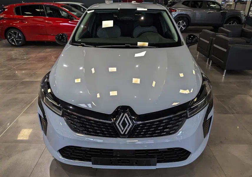Vue avant d'une Renault Clio V 2025 gris Rafale en showroom, avec calandre noire et logo Renault bien visible.