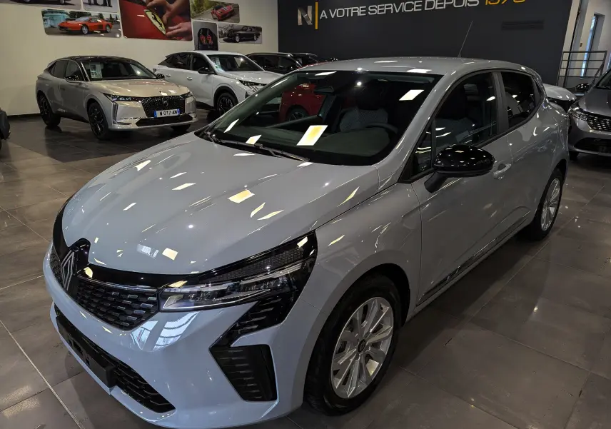 Renault Clio V Gris Rafale vue 3/4 avant droit en showroom, avec calandre noire et phares LED distinctifs.