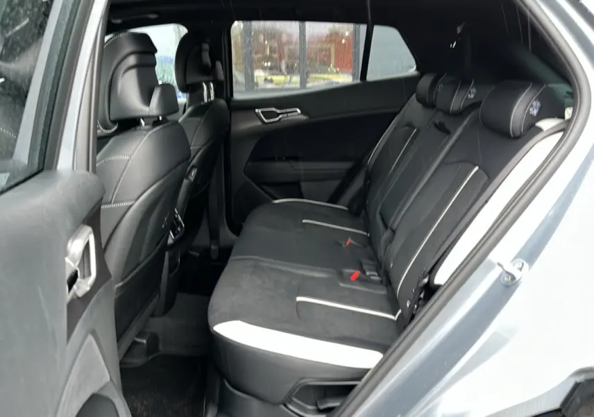 Vue intérieure arrière côté gauche du Kia Sportage 2026 gris perle, sièges noirs avec surpiqûres blanches.