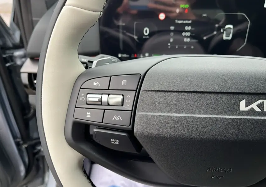 Gros plan sur le volant cuir clair du Kia Sportage 2026 avec commandes multifonctions et tableau de bord numérique flou.