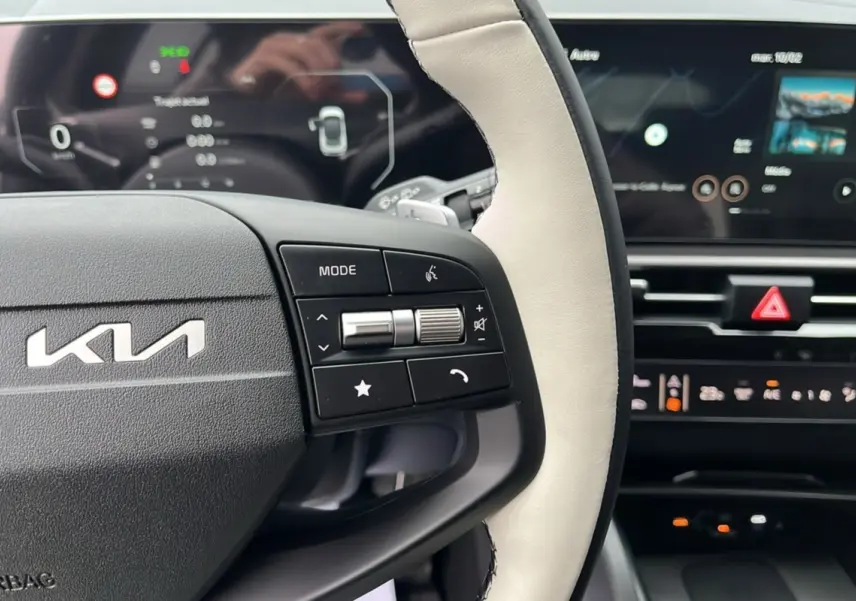 Vue rapprochée du volant cuir bicolore avec commandes multifonctions du Kia Sportage 2026, tableau de bord numérique en arrière-plan.