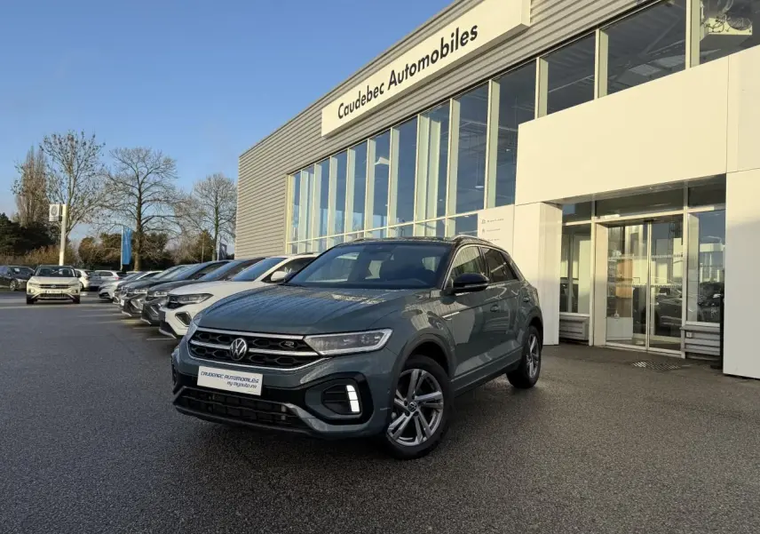 Volkswagen T-Roc bleu en 3/4 avant droit, stationné devant un concessionnaire Caudebec Automobiles.