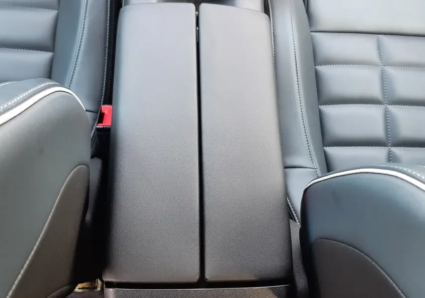 Vue plongeante sur l'accoudoir central noir et les sièges en cuir noir du Citroën C5 Aircross hybride 2026.