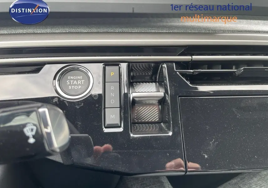 Gros plan sur la console centrale noire brillante du Peugeot 3008 Hybrid 2025 avec bouton start/stop et commandes de boîte auto.