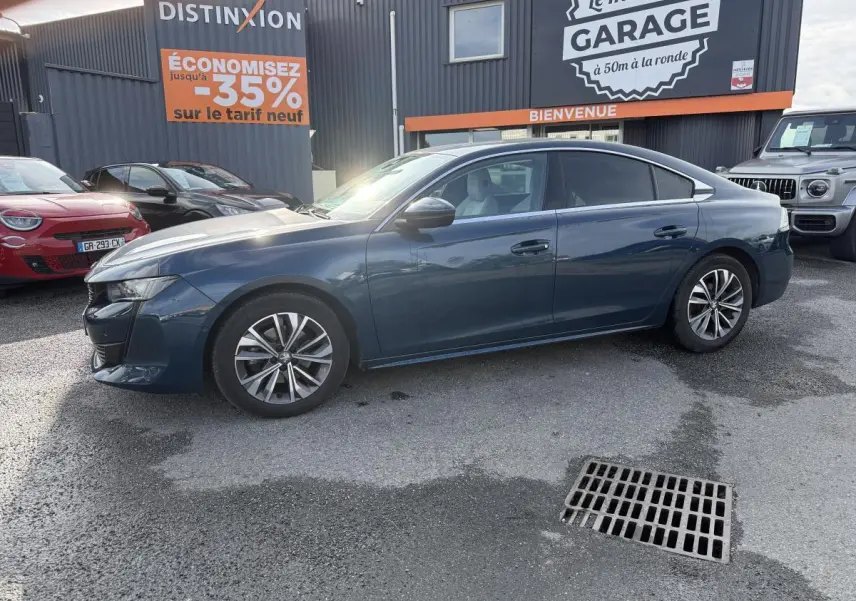 Peugeot 508 bleu métallisé vue de profil côté gauche, avec jantes alliage et vitres surteintées, stationnée devant un garage.