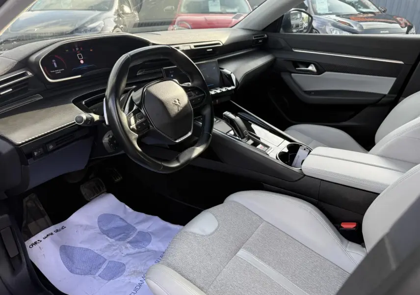 Vue intérieure côté conducteur du Peugeot 508 2019, avec sellerie gris clair et tableau de bord noir à inserts carbone.