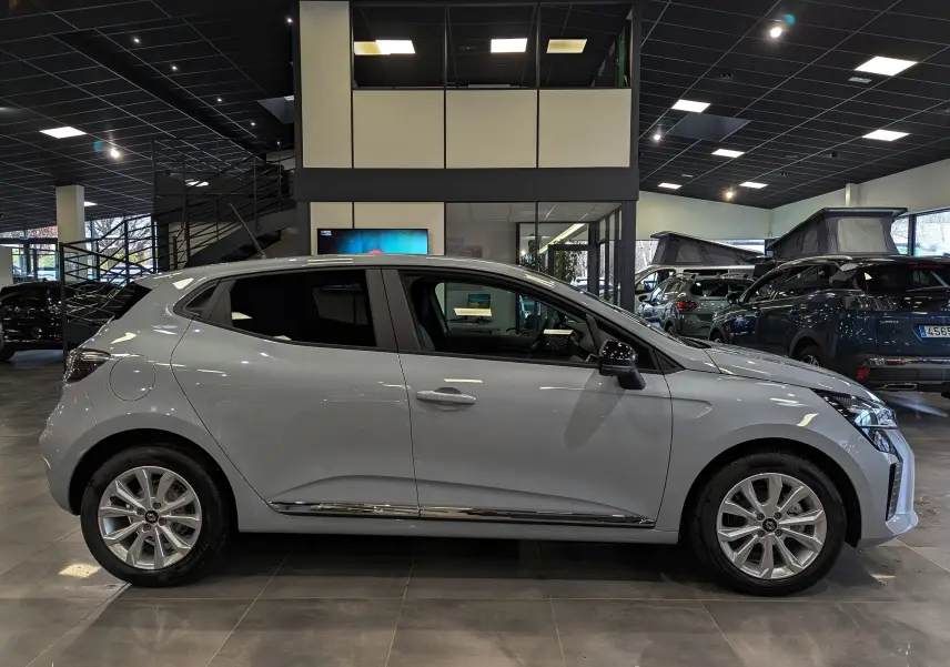 Profil latéral droit d'une Renault Clio V 2025 gris Rafale en showroom, avec jantes alliage et vitres teintées.