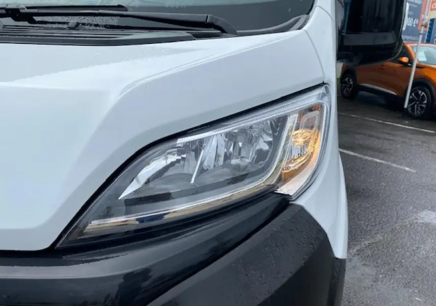 Gros plan sur le phare avant droit du fourgon blanc Opel Movano 2023, avec pare-chocs noir et rétroviseur visible.