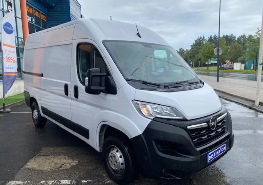 Vue 3/4 avant droit d’un Opel Movano Fourgon blanc avec porte latérale coulissante, stationné sous un ciel couvert.