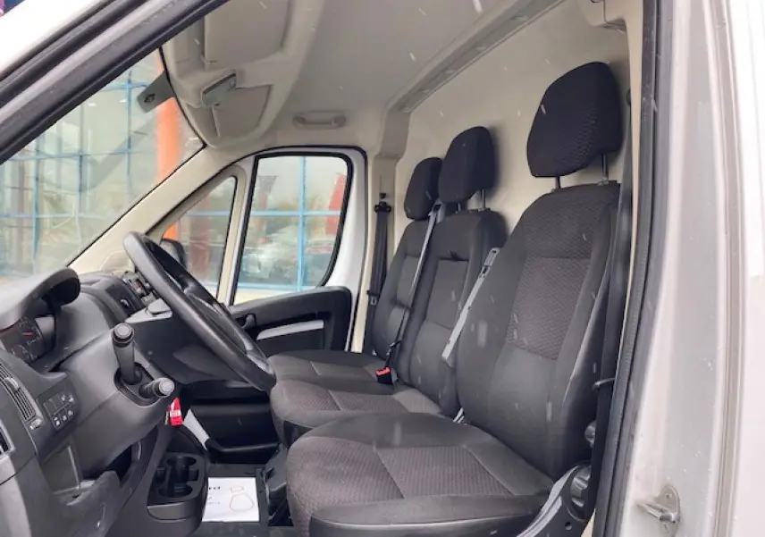 Vue intérieure côté conducteur de l'Opel Movano Fourgon blanc, montrant la banquette 3 places et le volant.
