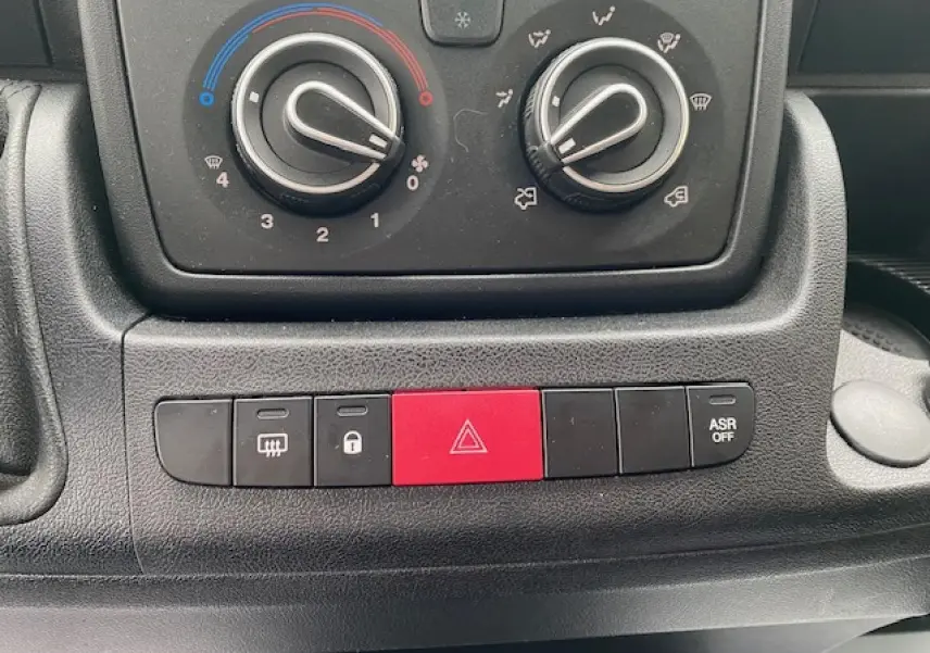 Gros plan sur les commandes de climatisation et les boutons de sécurité du tableau de bord noir de l’Opel Movano Fourgon 2023.