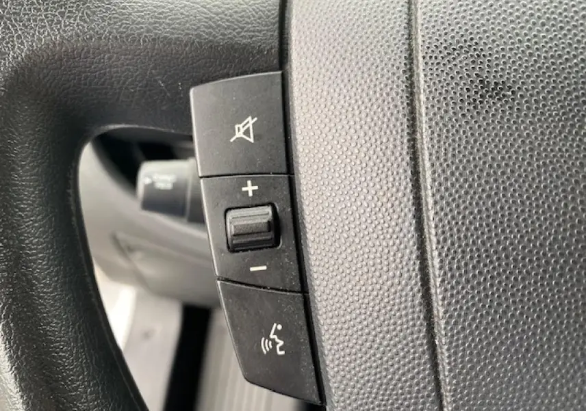 Gros plan sur les commandes de volume et de coupure du son au volant du fourgon blanc Opel Movano 2023.