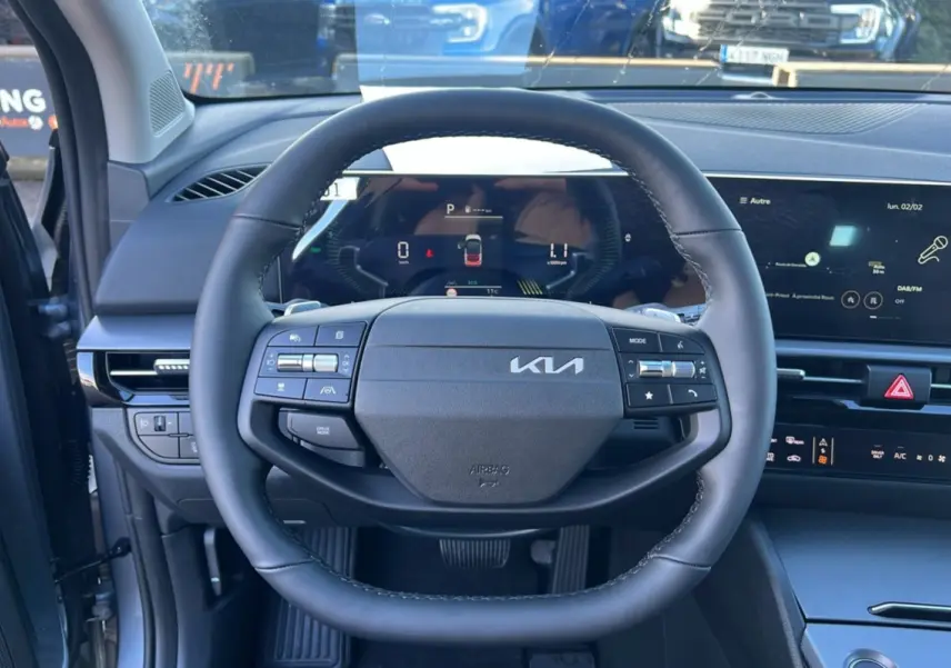 Vue intérieure centrée sur le volant cuir multifonctions du Kia Sportage 1.6 T-GDI HEV gris perle avec tableau de bord digital.