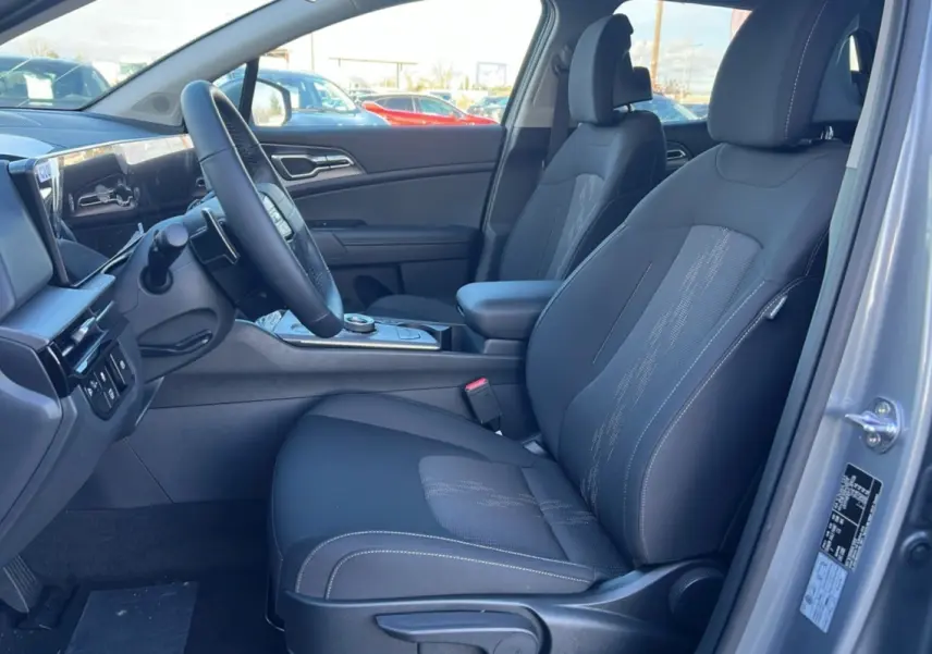 Vue intérieure côté conducteur du Kia Sportage gris perle 2026, sièges tissu noirs avec console centrale et volant multifonctions.