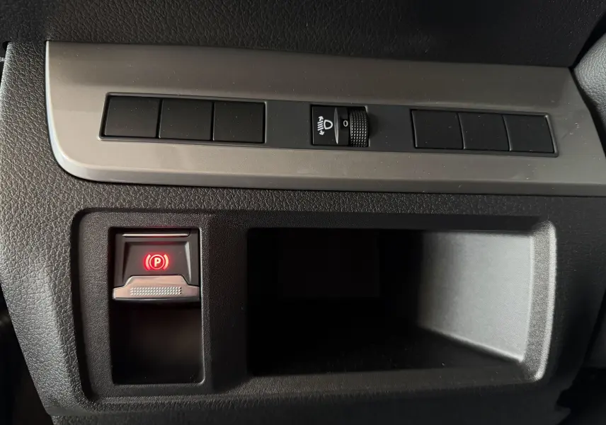 Gros plan sur la commande de frein à main électrique rouge et le réglage des phares sur le tableau de bord noir du Citroën Jumpy Gris Titane.