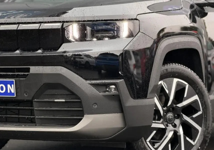 Gros plan sur l'avant droit noir Vulcano du Jeep Compass Hybrid 145 e-DSC6 avec jante alliage 19 pouces et phares LED allumés.