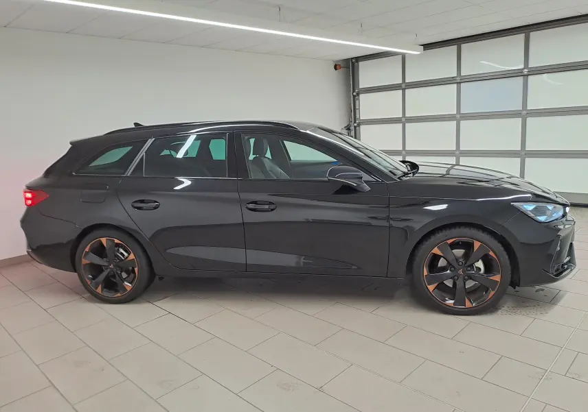 Vue de profil côté gauche d'une CUPRA LEON ST 2025 noire minuit avec jantes alliage 18'' cuivrées en intérieur lumineux.