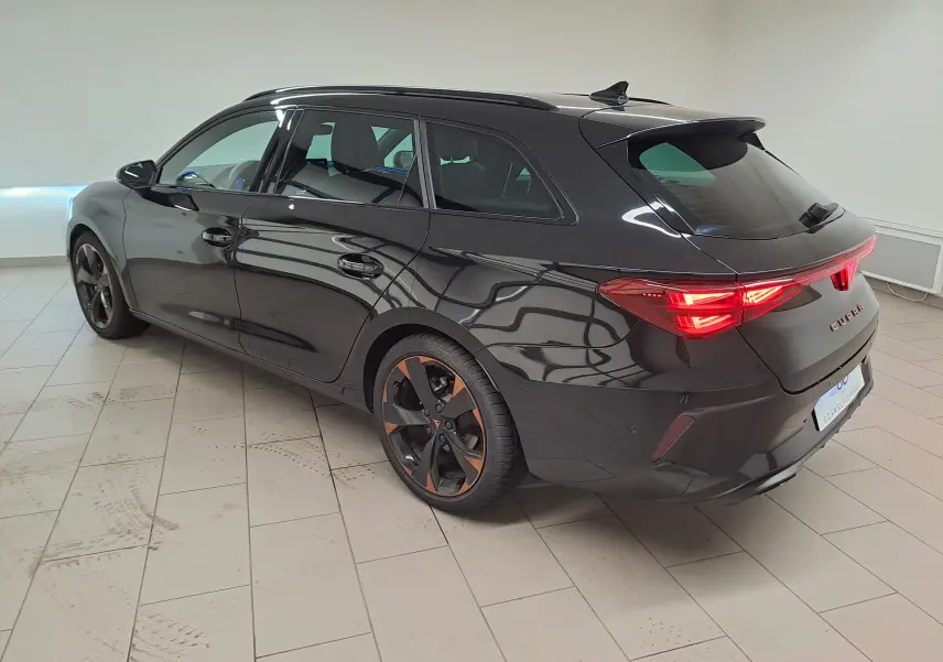Vue 3/4 arrière droite de la CUPRA Leon ST 1.5 eTSI noire Minuit avec jantes alliage 18'' cuivrées et feux arrière allumés.