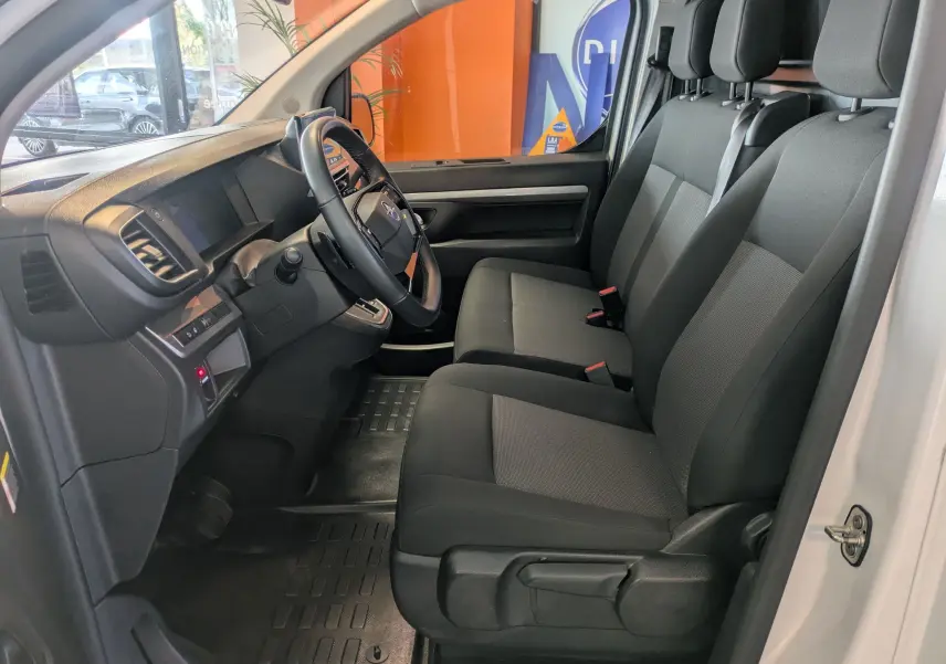 Vue intérieure côté conducteur de l'Opel Vivaro Fourgon blanc Icy 2024, montrant les sièges avant et le tableau de bord.