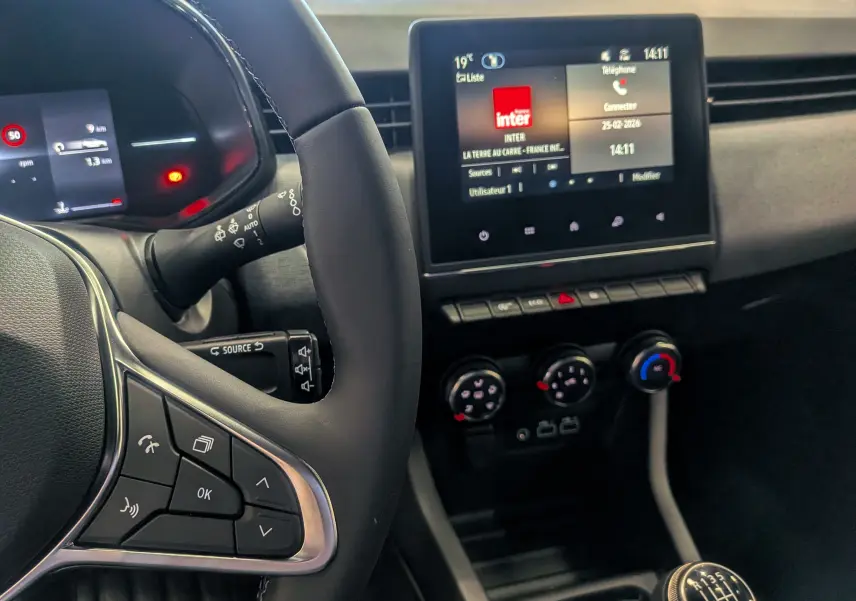 Vue intérieure centrée sur le volant et la console centrale de la Renault Clio V Blue dCi 100 CH Evolution, avec écran tactile et levier de vitesse manuel.