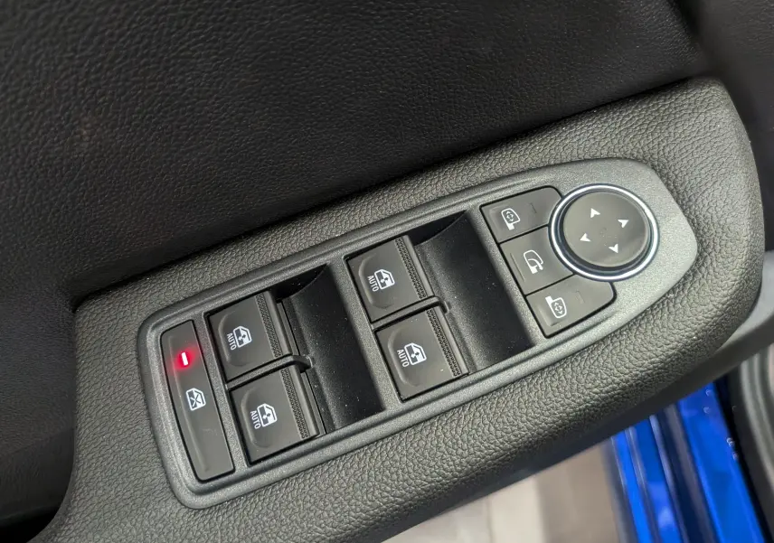 Gros plan sur les commandes des vitres électriques et rétroviseurs côté conducteur, avec bordure de porte bleu Iron visible.