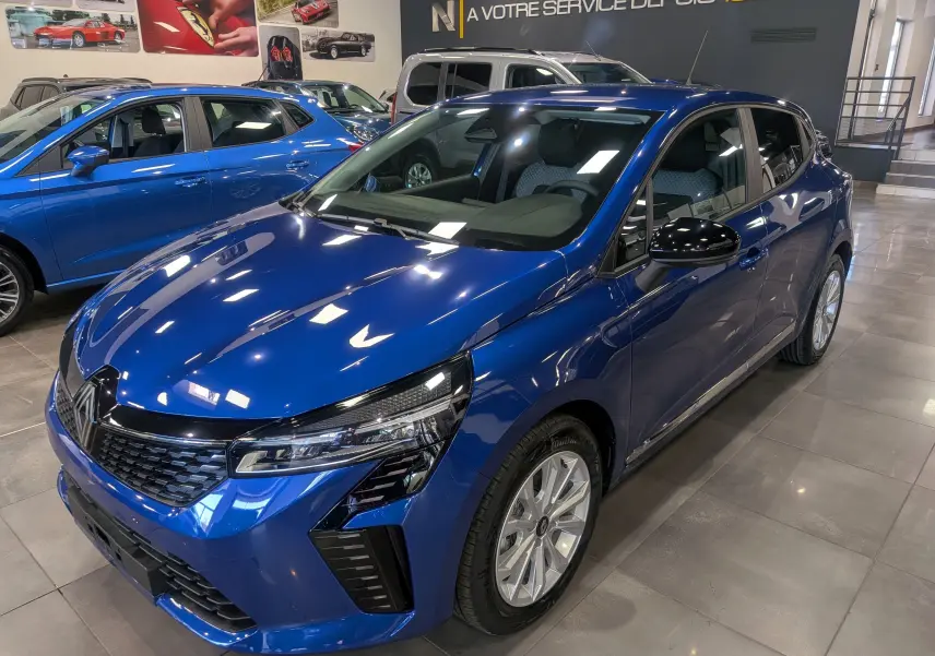 Renault Clio V Bleu Iron vue 3/4 avant droit en concession, avec jantes alliage et rétroviseurs noirs.