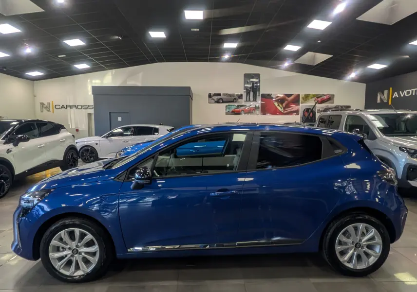 Profil droit d'une Renault Clio V bleu Iron 2025 en finition Evolution, visible en intérieur de showroom lumineux.