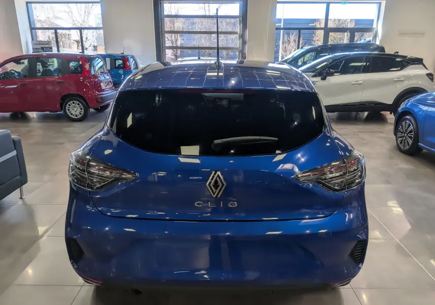 Vue arrière d'une Renault Clio V Bleu Iron 2025 dans un showroom, avec feux arrière modernes et vitre arrière teintée.