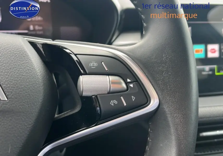 Gros plan sur les commandes multifonctions à gauche du volant cuir d'une Skoda Fabia bleu, avec écran tactile en arrière-plan.