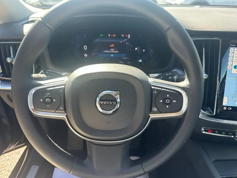 Vue rapprochée du volant multifonction noir de la Volvo S60 2024 avec tableau de bord numérique et écran tactile latéral.