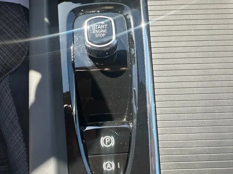 Gros plan sur la console centrale noire brillante du Volvo S60 B4 2024 avec bouton Start Engine Stop et commandes de frein à main.