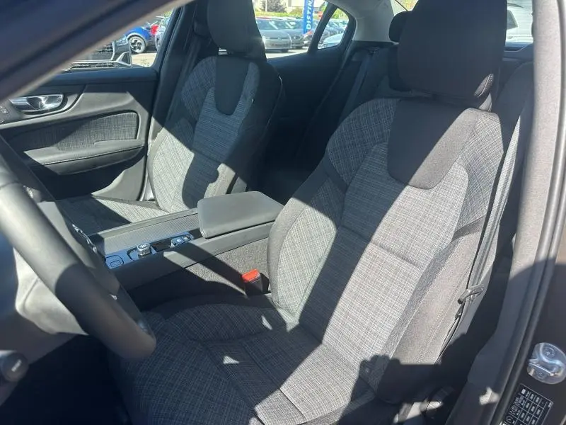 Vue intérieure côté droit des sièges avant en tissu gris à motifs, avec accoudoir central et console d'une Volvo S60 gris Platinium 2024.
