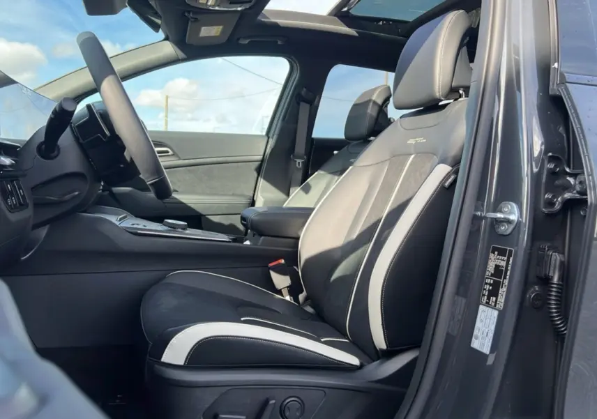 Vue intérieure côté conducteur du Kia Sportage 2026 gris eclipse avec sièges sport noirs et toit panoramique ouvert.