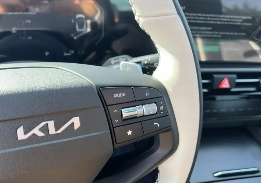 Gros plan sur le volant cuir blanc et noir du Kia Sportage 2026 avec commandes multifonctions et tableau de bord numérique flou.