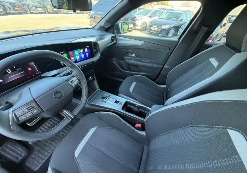 Vue intérieure côté conducteur de l’Opel Mokka électrique 2025, montrant le volant, écran tactile et sièges noirs avec surpiqûres grises.