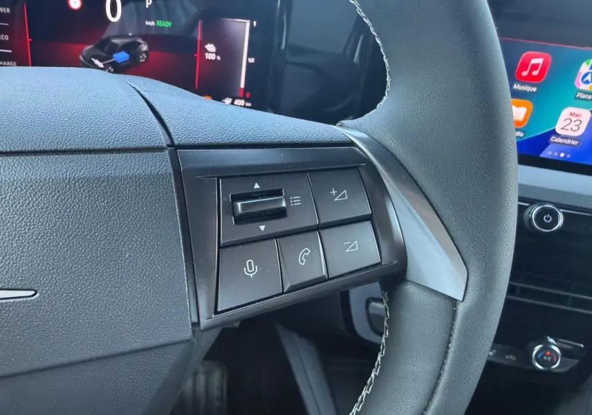 Gros plan sur les commandes au volant côté gauche de l’Opel Mokka électrique 2025, avec écran tactile en arrière-plan.