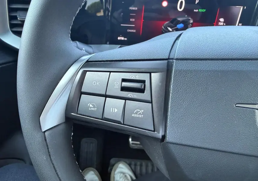 Gros plan sur les commandes à gauche du volant noir de l’Opel Mokka électrique 2025 avec écran numérique en arrière-plan.