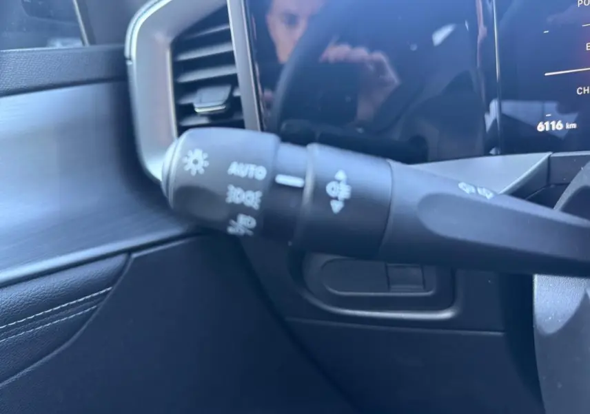 Gros plan sur la commande des phares à gauche du volant dans l'habitacle noir de l'Opel Mokka électrique 2025.