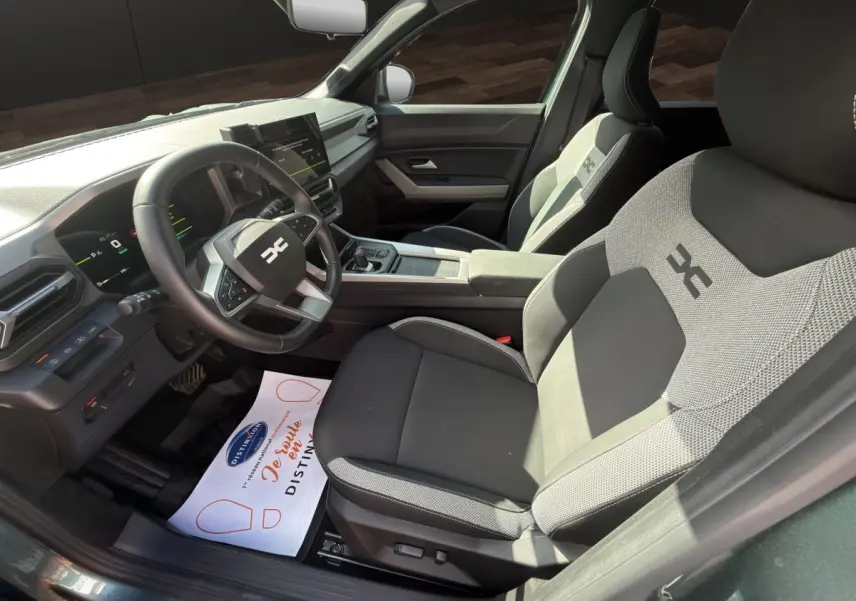 Vue intérieure côté conducteur du Dacia Bigster Journey hybride vert 2025, avec sièges tissu bicolore et volant multifonctions.