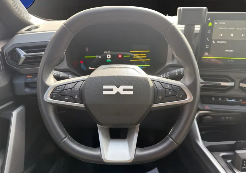 Vue intérieure centrée sur le volant cuir noir du Dacia Bigster Journey Hybrid 2025 avec tableau de bord numérique et écran tactile.