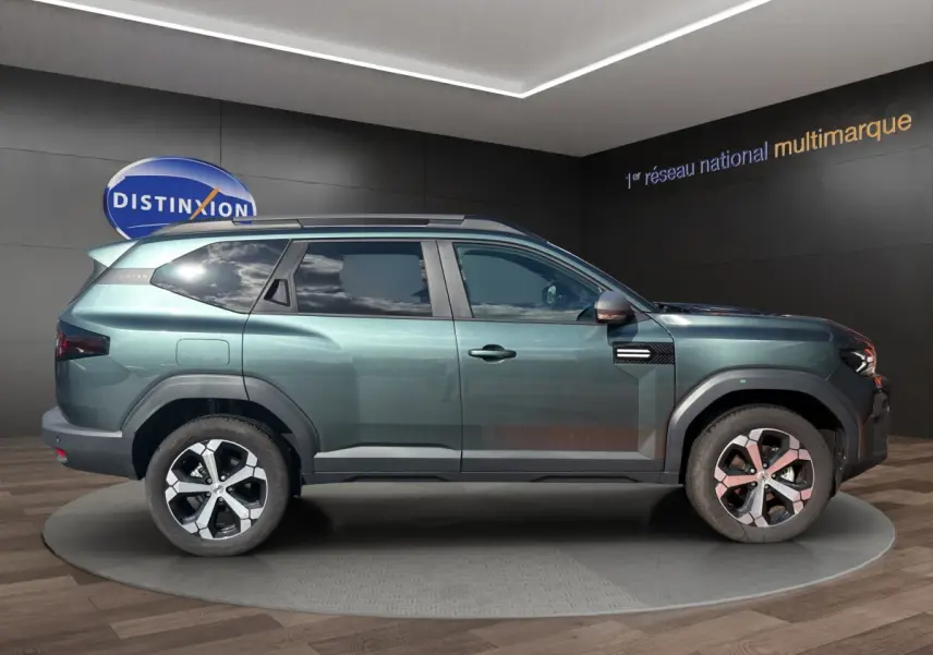 Vue de profil côté gauche du SUV Dacia Bigster vert métallisé avec attelage RDSO, roues alliage et barres de toit noires.