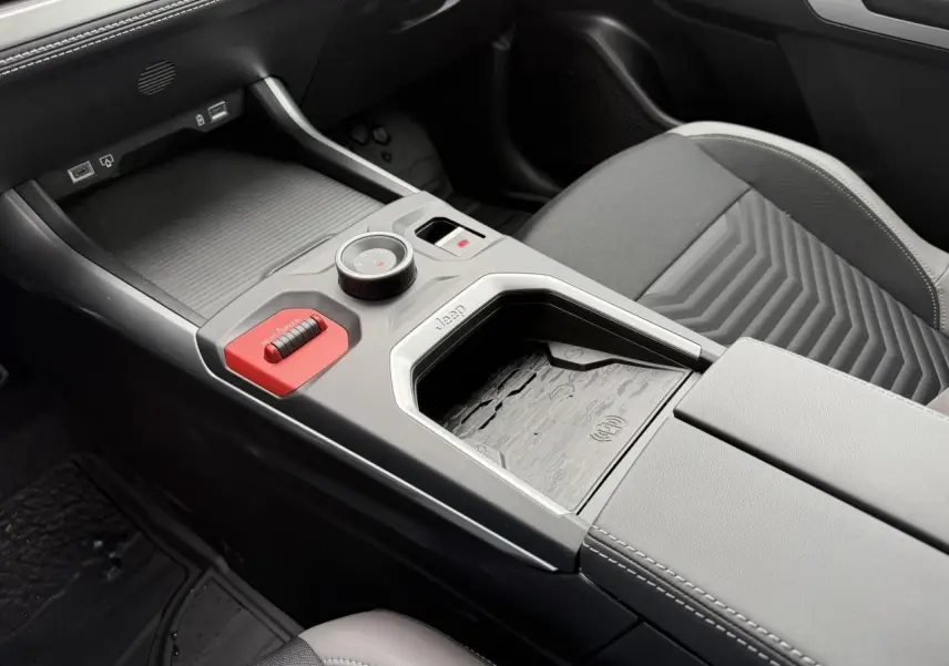 Gros plan sur la console centrale intérieure du Jeep Compass 2026, avec sellerie mixte gris et chargeur sans fil visible.