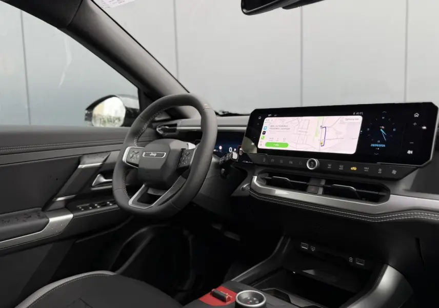 Intérieur du Jeep Compass 2026 vu côté conducteur, tableau de bord noir avec écran tactile large affichant la navigation.