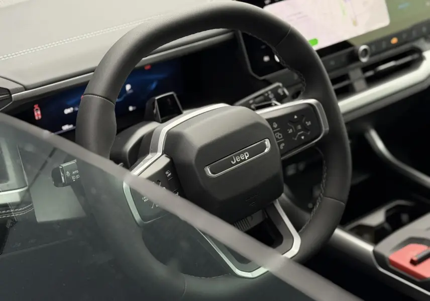 Vue rapprochée du volant noir du Jeep Compass 2026 avec tableau de bord numérique et écran tactile visible en arrière-plan.