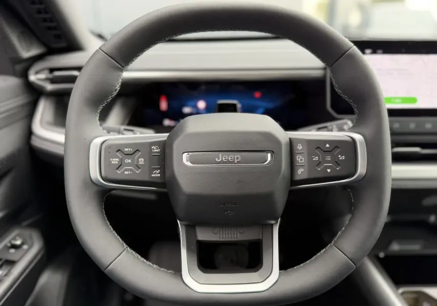 Vue rapprochée du volant noir du Jeep Compass 2026 avec commandes intégrées et tableau de bord numérique flou.